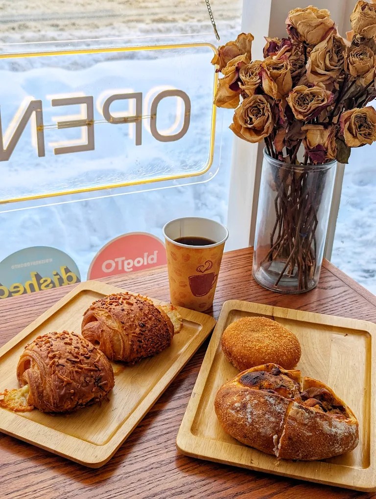 Wooden table with pastries, takeaway coffee, dried branches, snowy College Street through the window