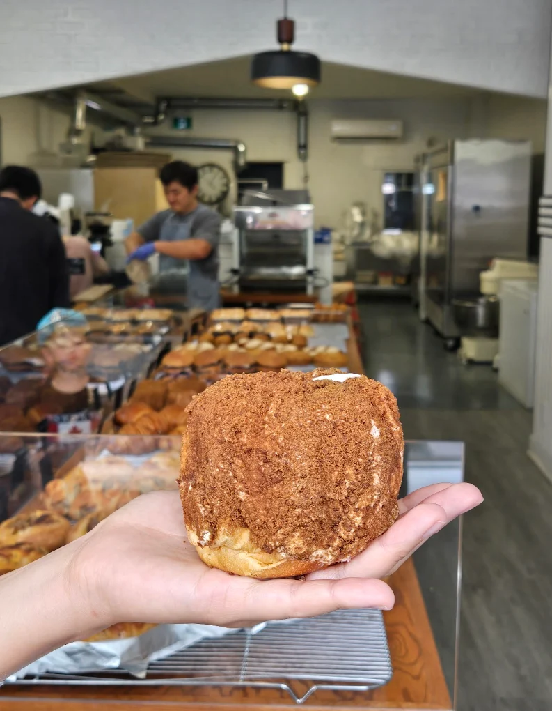 Hand holding a round crumb-coated pastry in front of the bakery display case